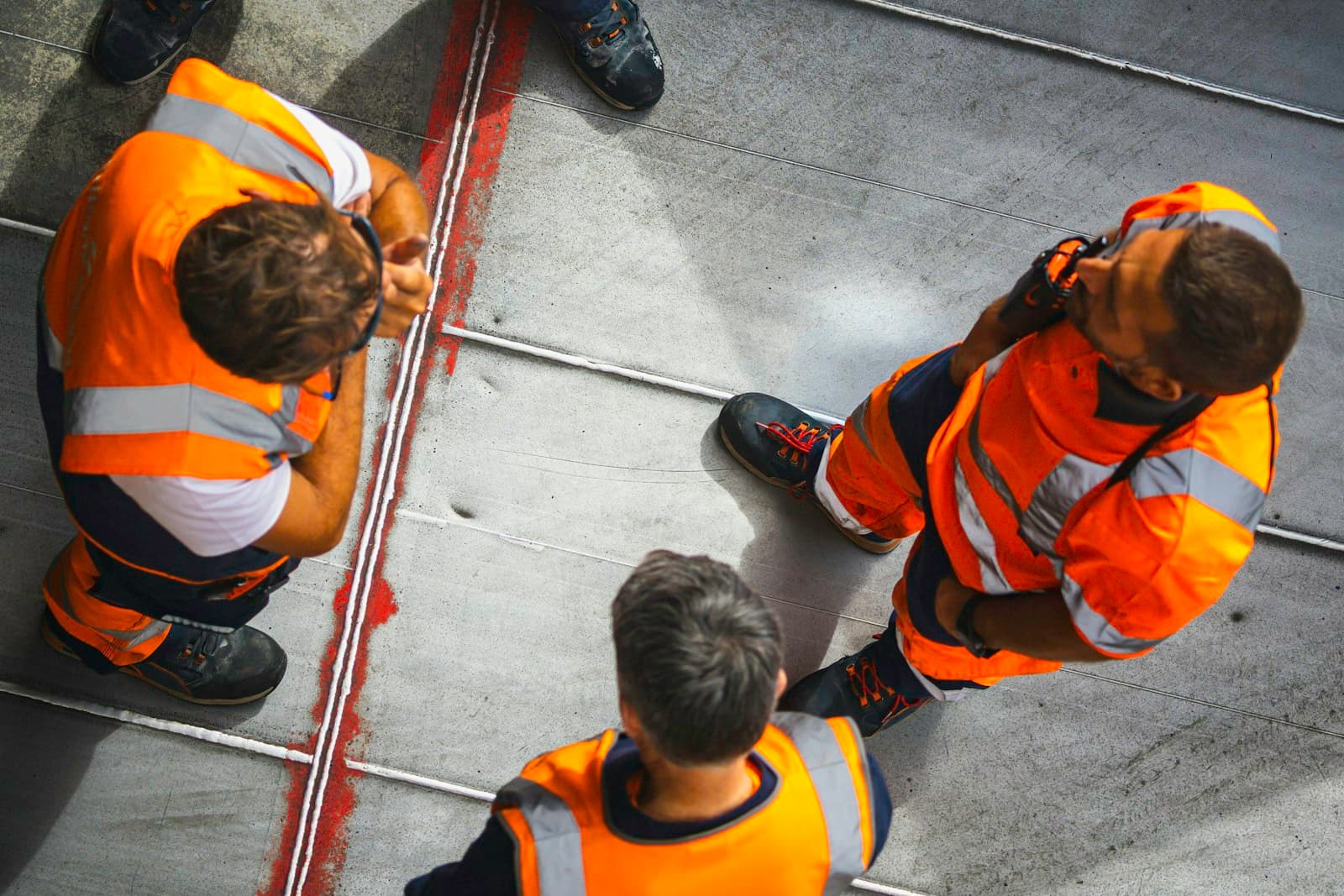 Vier medewerkers in oranje veiligheidshesjes overleggen op locatie